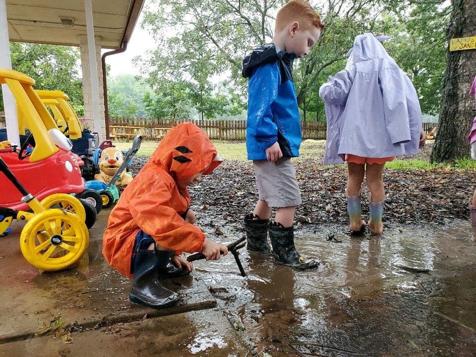 Three children in rain gear playing in puddles