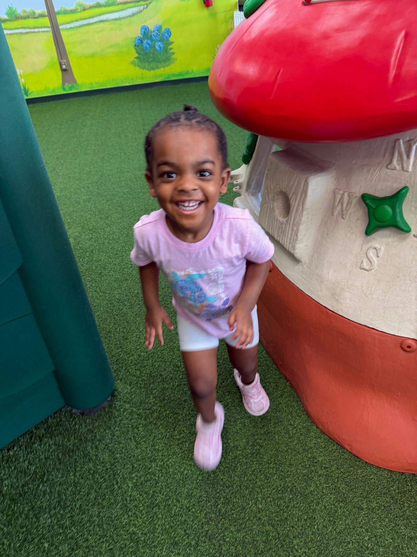 Child smiling while standing on a green play surface