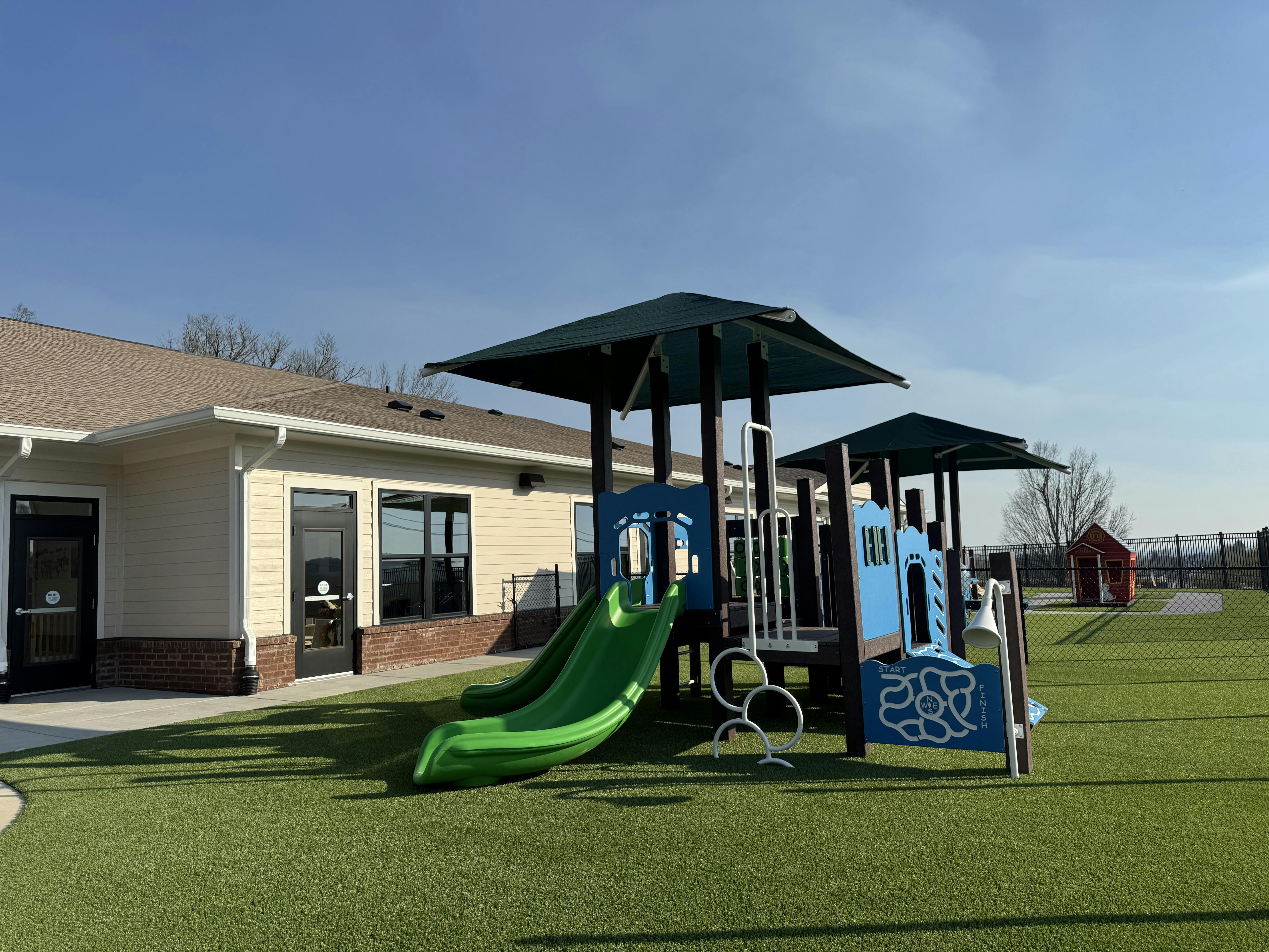 Playground structure with slides on an artificial turf field next to a building