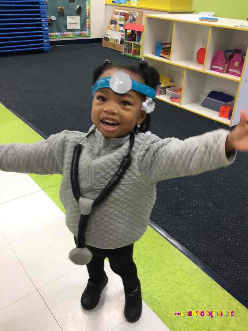 Child wearing a doctor's head mirror and stethoscope in a classroom
