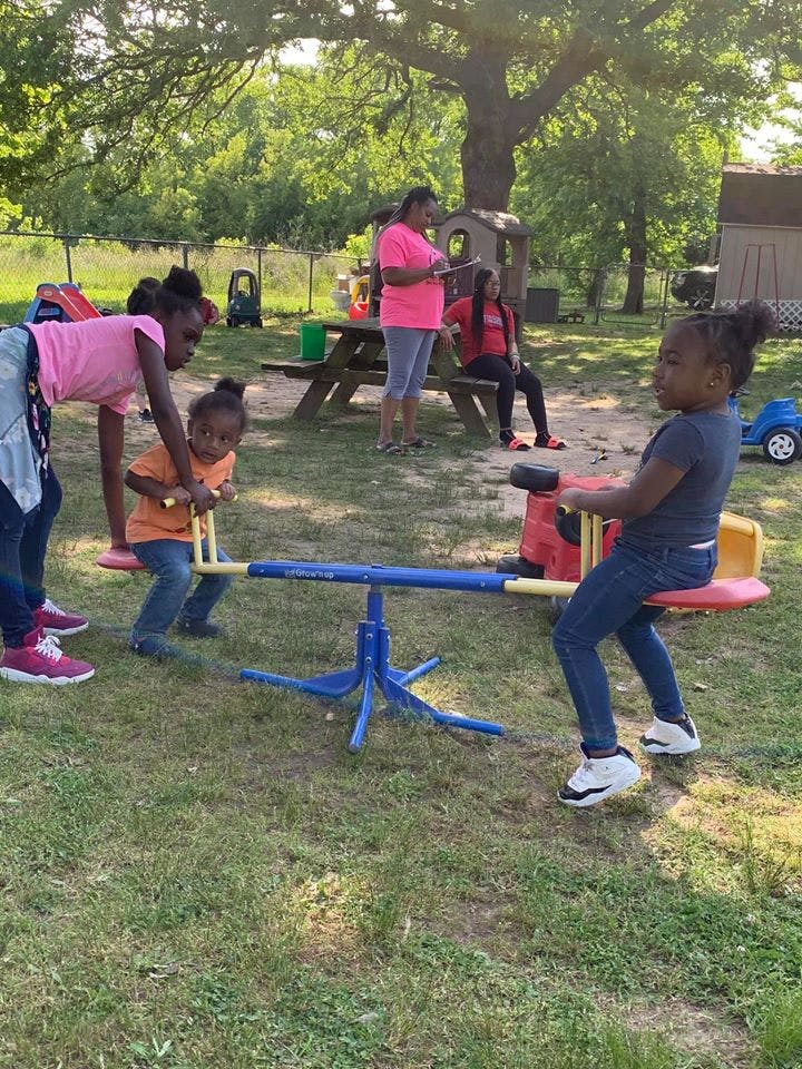 Two children playing on a seesaw with adults in the background