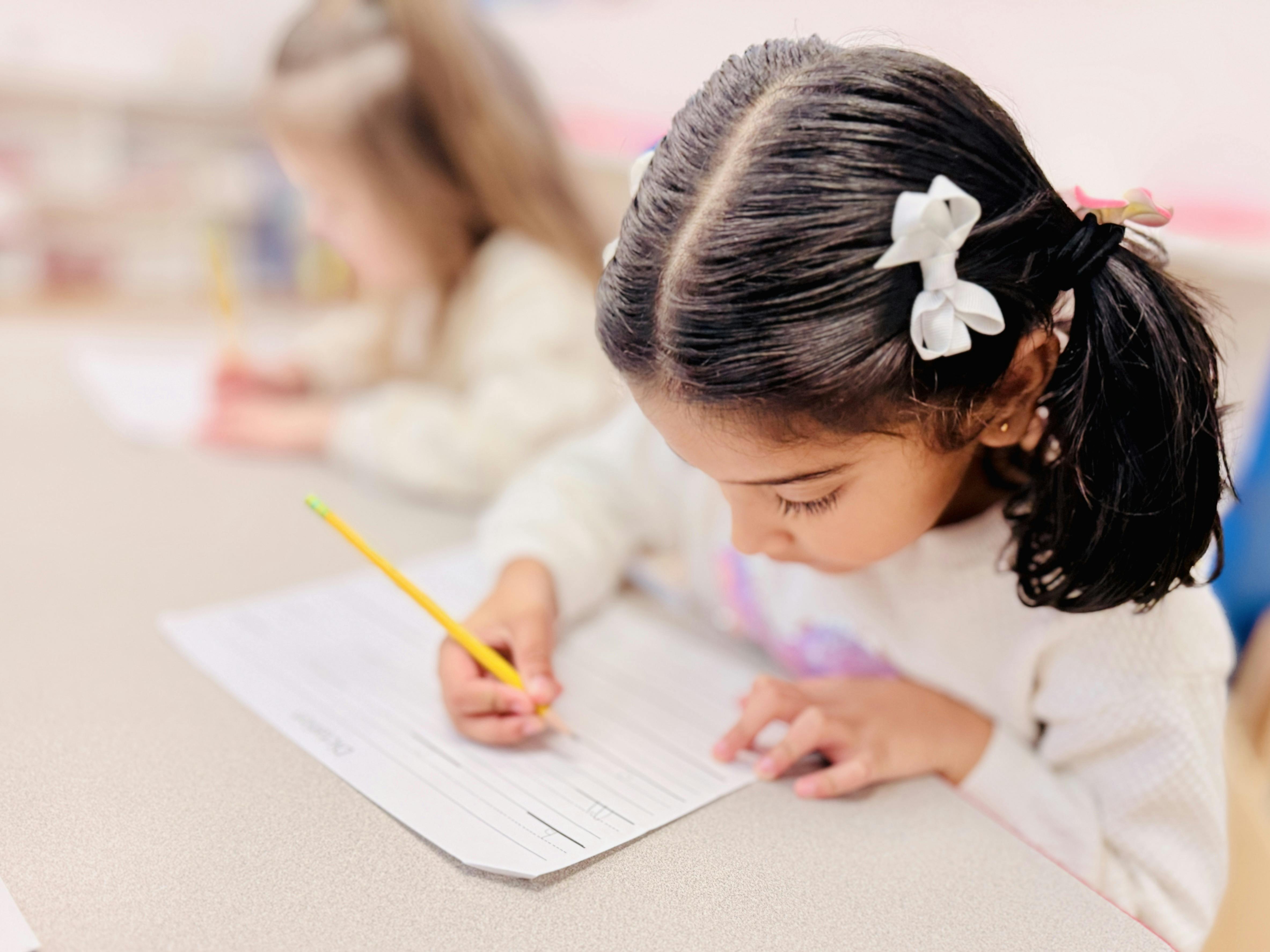 Child writing on paper with a pencil in a classroom