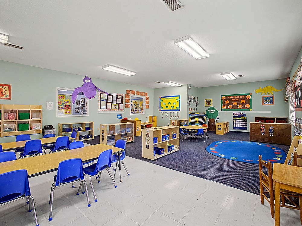 Empty classroom with small tables and blue chairs on linoleum and carpet flooring