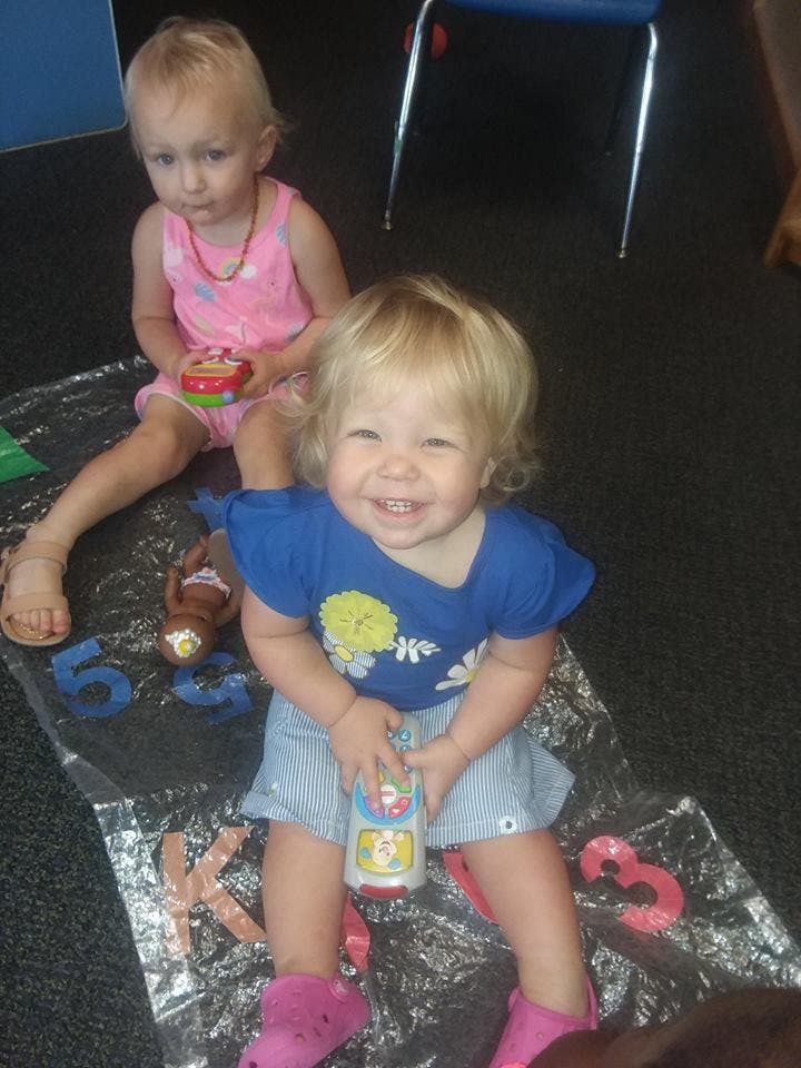 Two children sitting on the floor, one smiling at the camera