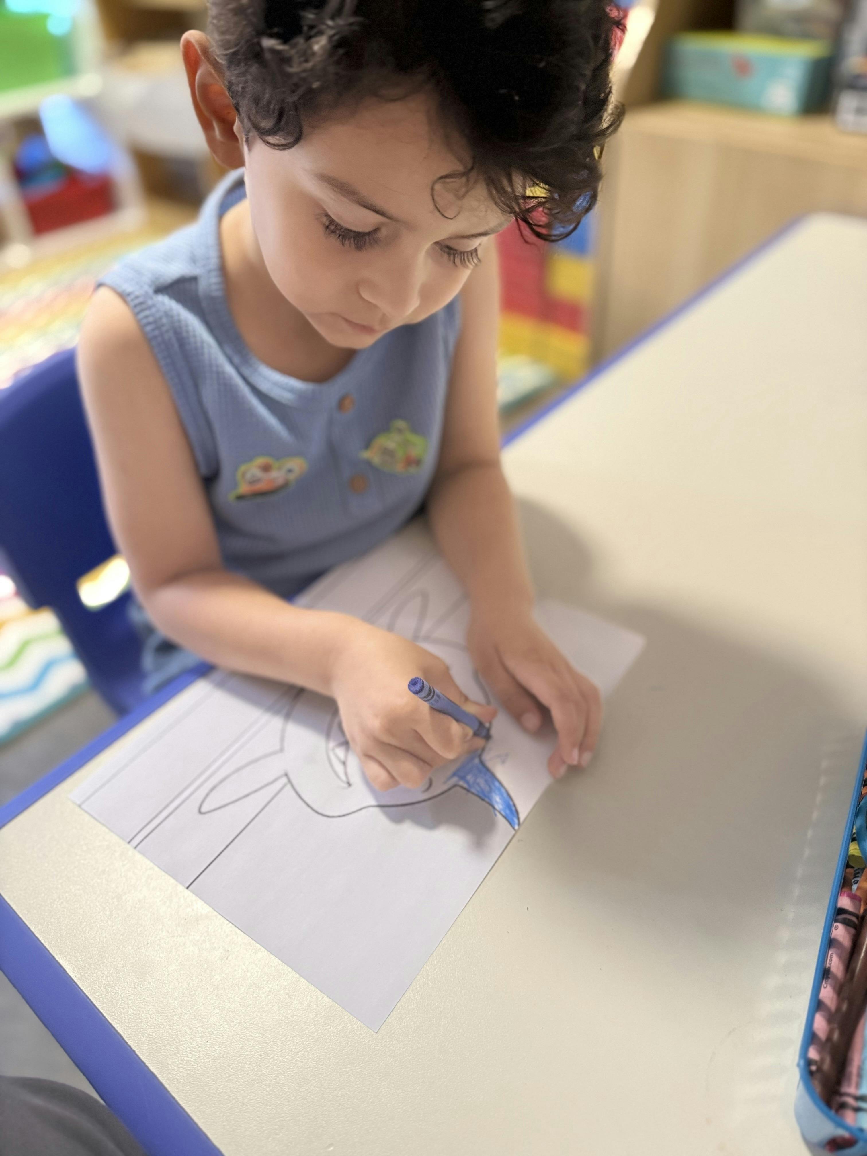 Child coloring with a blue crayon at a table