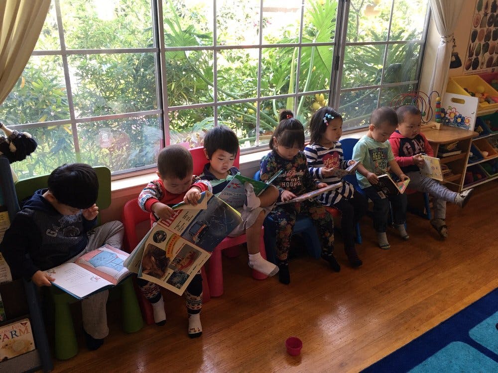 Children sitting in a row reading books in a classroom