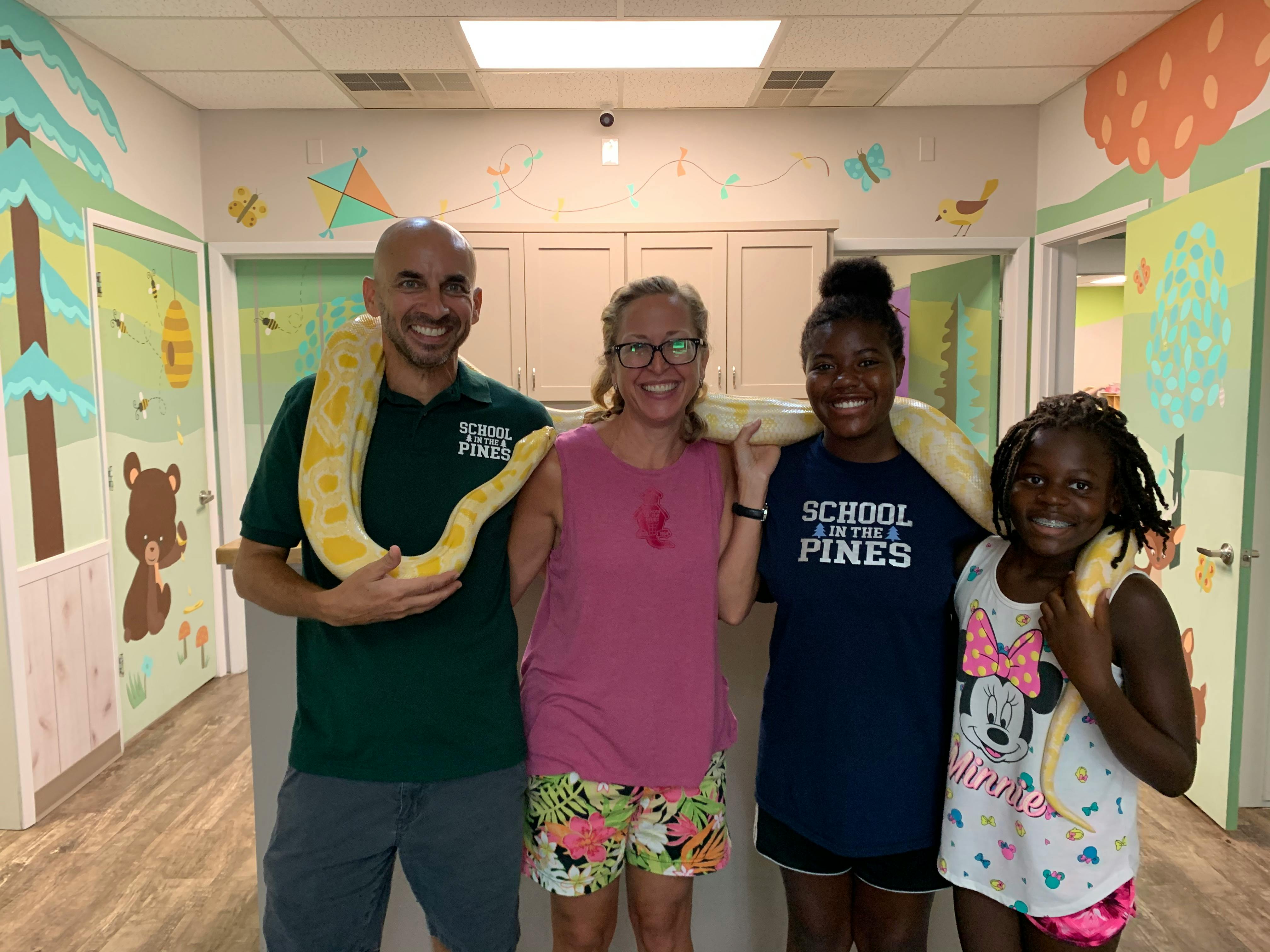 Four people and two children holding a large snake