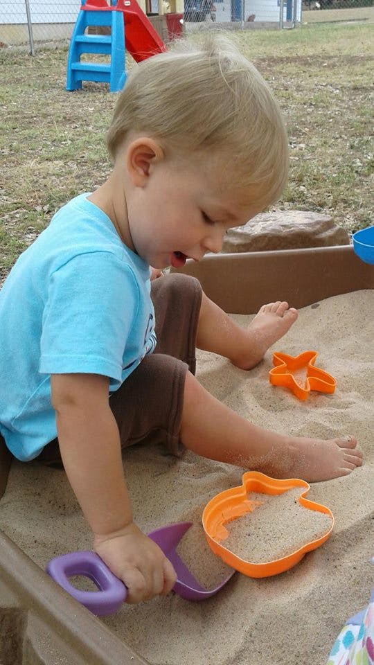 Child playing in a sandbox with a shovel and sand toys