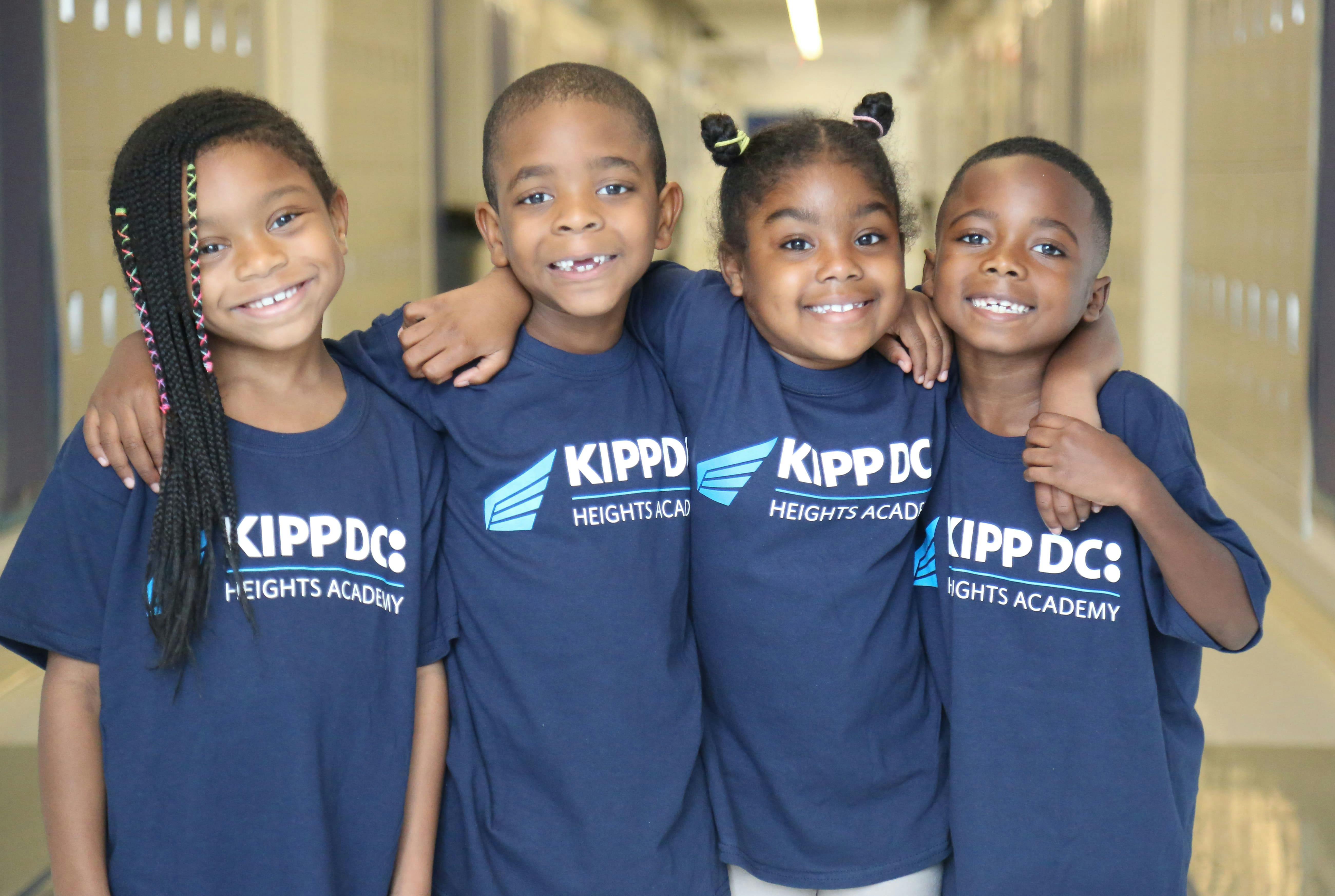 Four children in matching navy school shirts standing together in a hallway