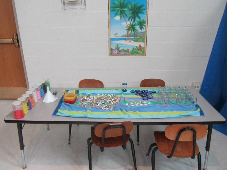 Table with craft supplies, including colorful sand, funnels, and small objects