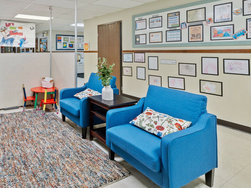 Lounge area in a school hallway with two blue armchairs and a small children's table