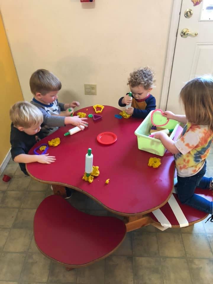 Four children playing with modeling clay at a red table