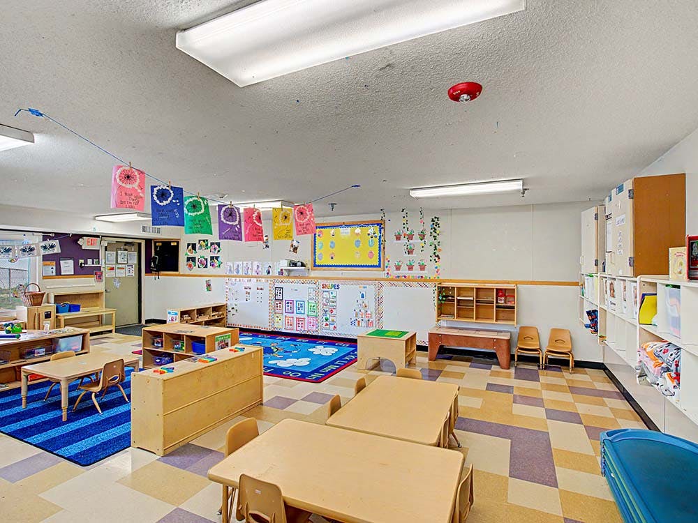 Classroom with small tables, chairs, colorful rugs, and decorations