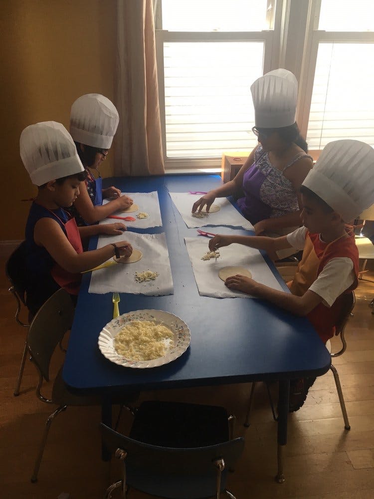 Children and an adult in chef hats making food at a table