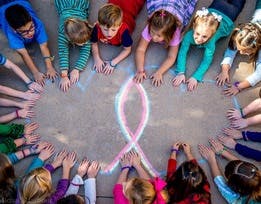 Children making a circle with their hands around a chalk drawing