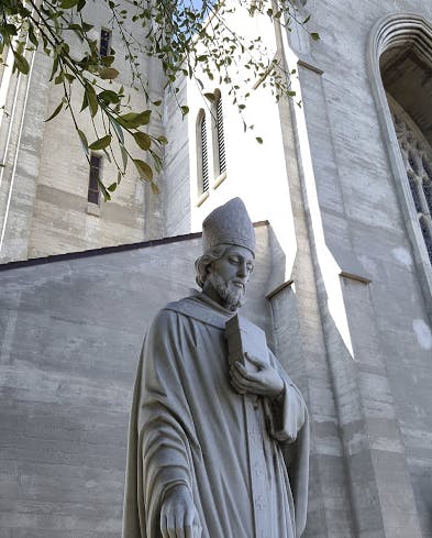 Stone statue of a person in a robe and hat holding a book