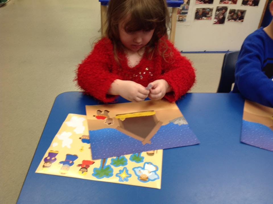 Child in a red sweater working on a craft at a blue table