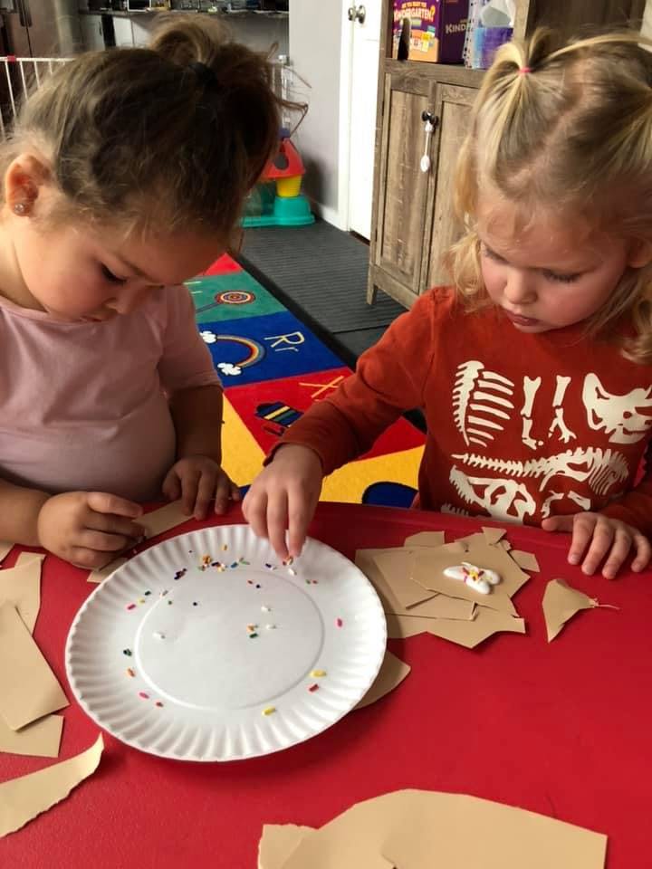 Two children decorating paper cutouts with sprinkles