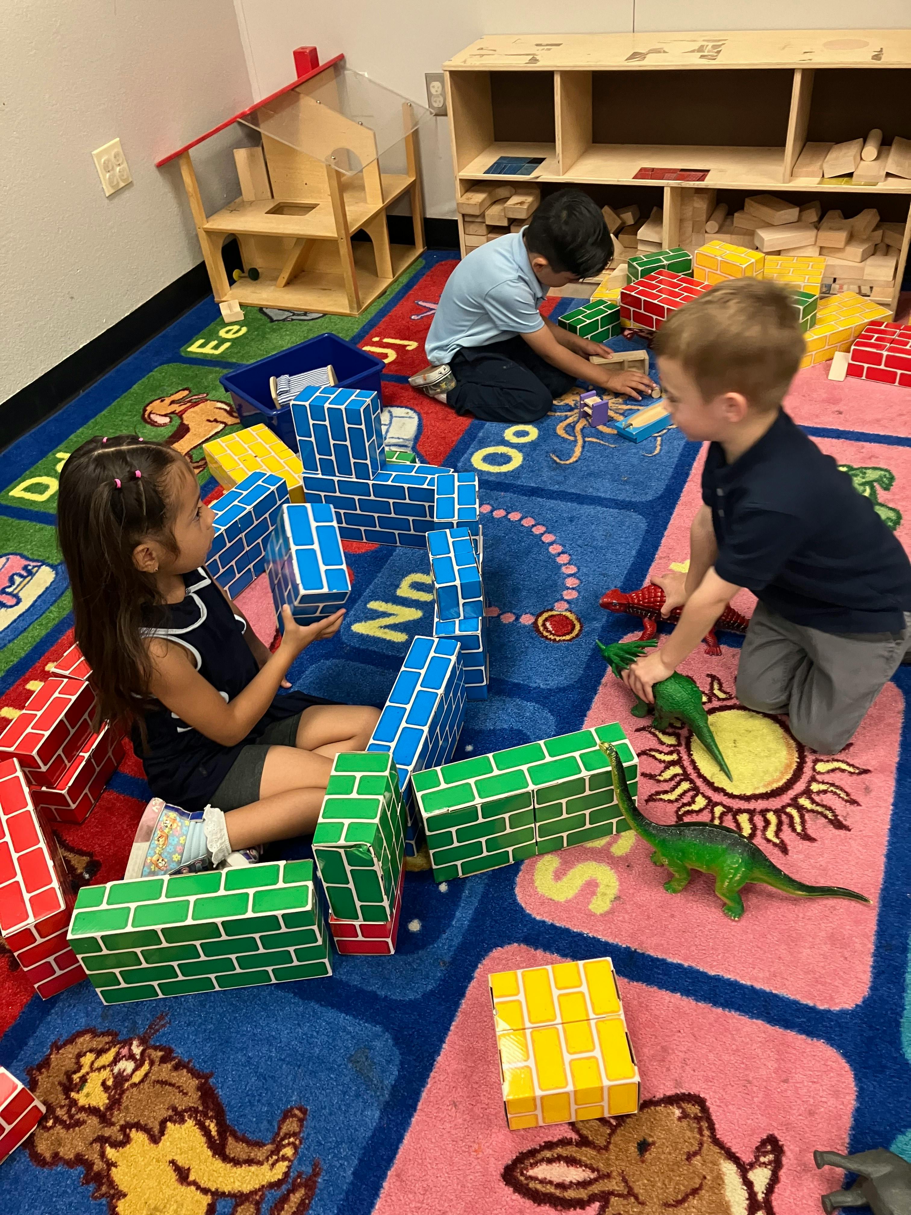 Three children playing with large building blocks on a colorful rug