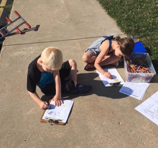 Two children drawing on paper outdoors