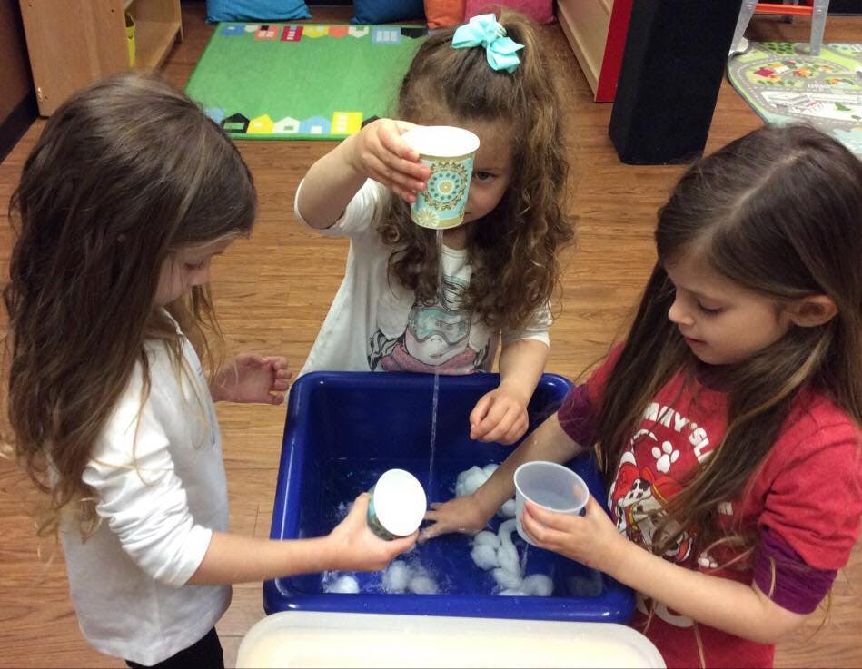 Three children playing with cups and water in a blue bin