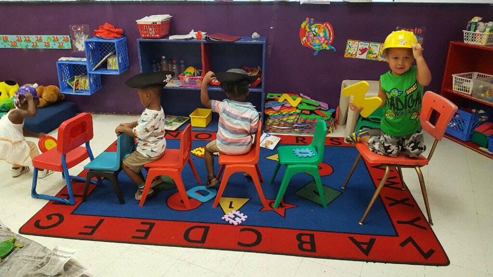 Children in a classroom, one child wearing a yellow hard hat