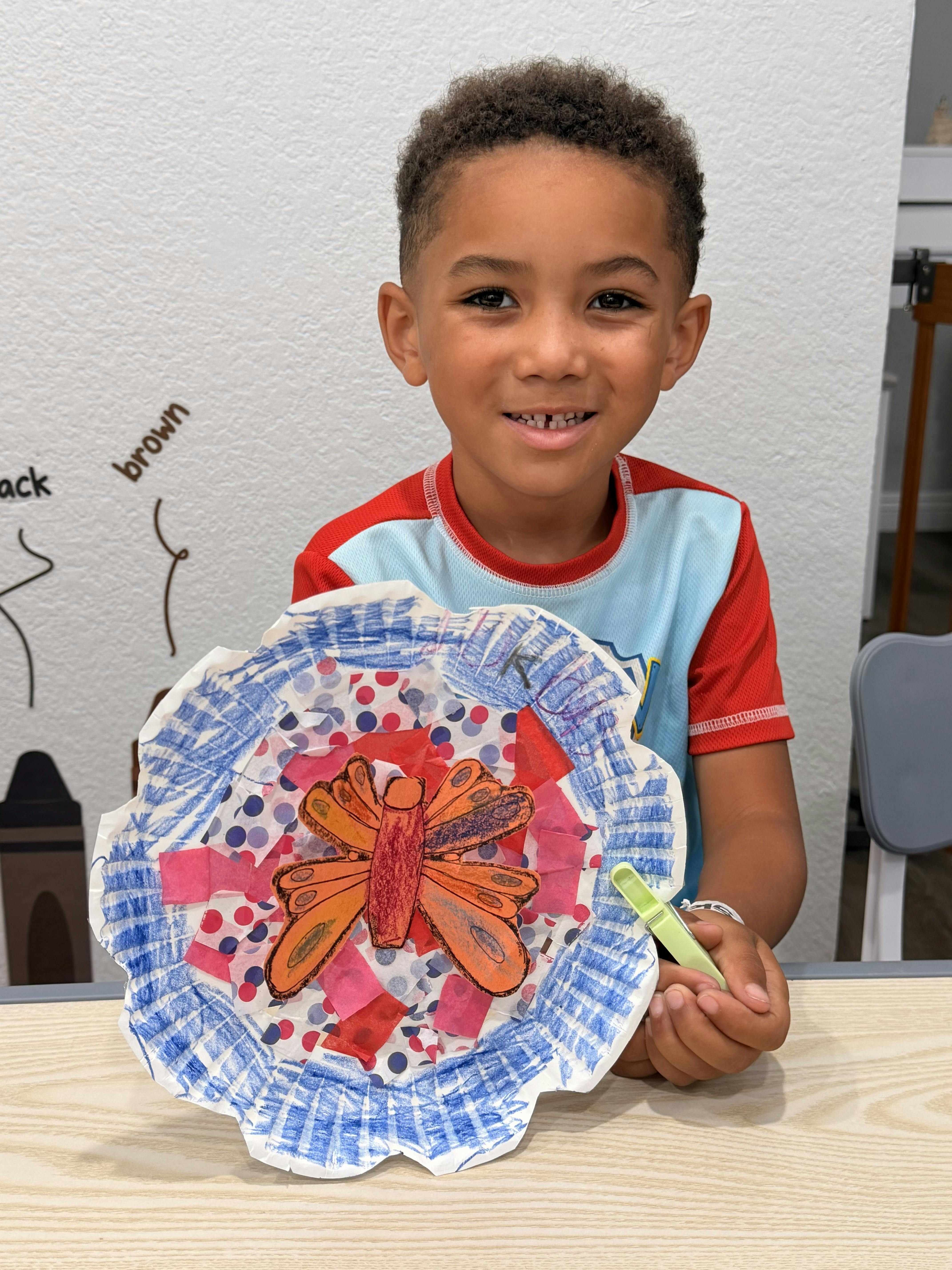 Child holding a butterfly paper craft at a table