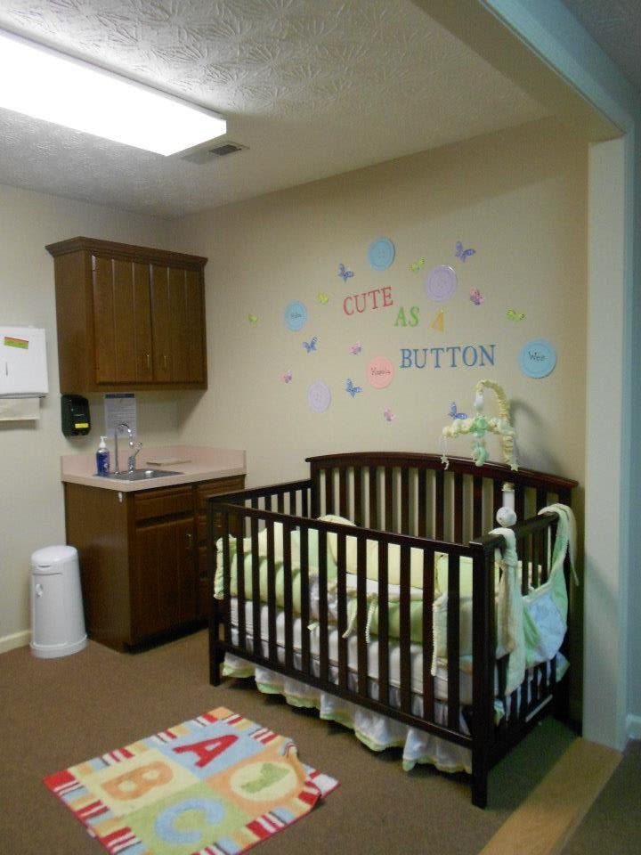 Nursery room with a crib, sink, and wall decor that says "Cute as a Button"