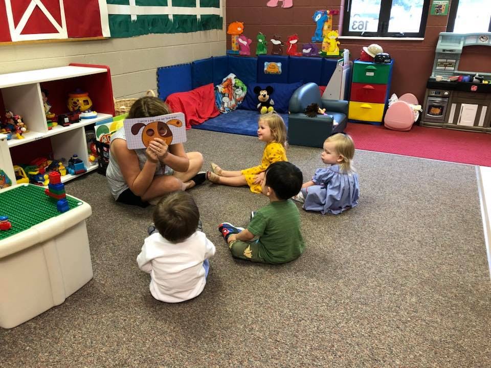 Person reading a book to four children in a classroom