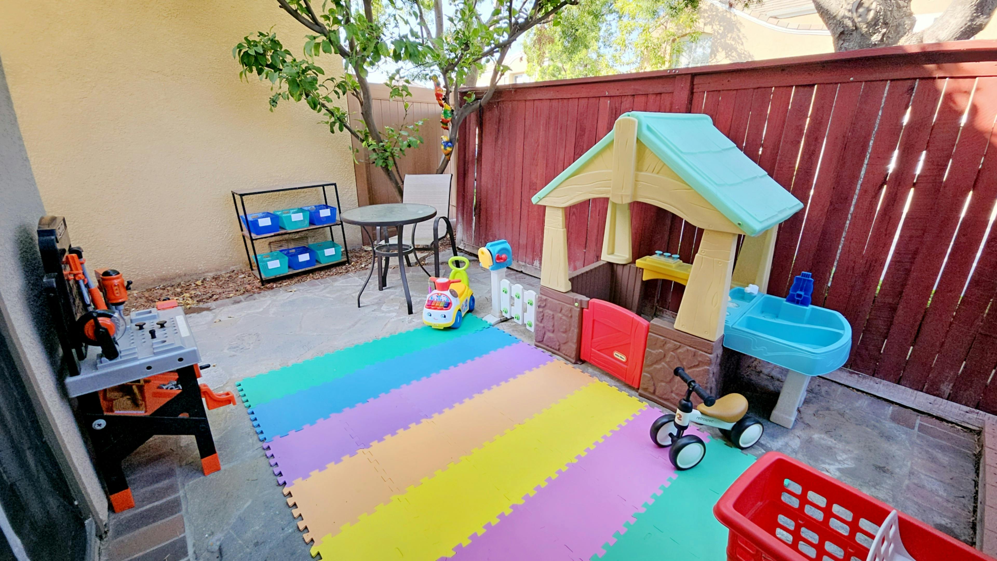 Outdoor play area with colorful mat, playhouse, and toys