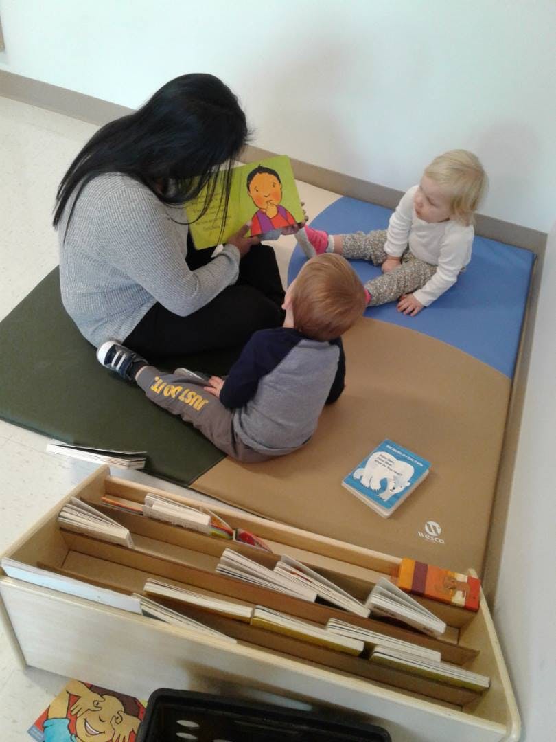 Person reading a book to two children on a mat