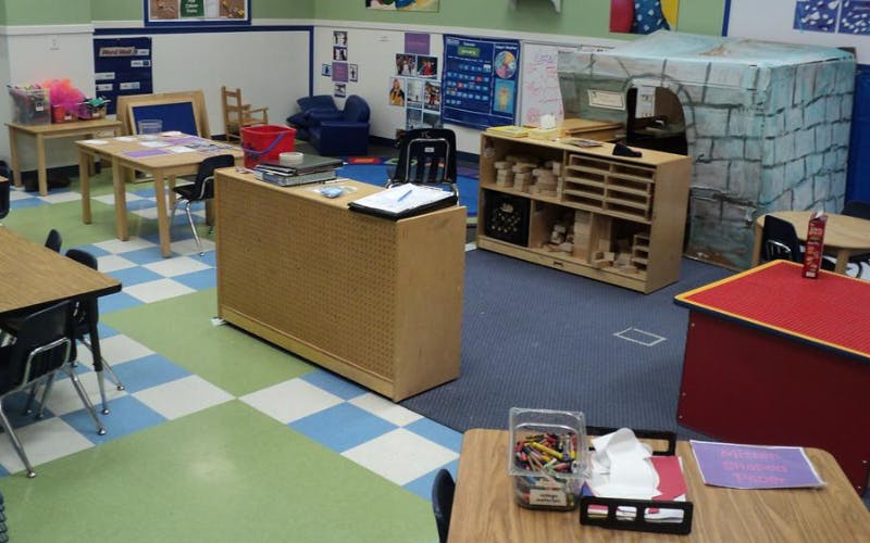 Classroom with tables, chairs, shelving units, and a cardboard fort