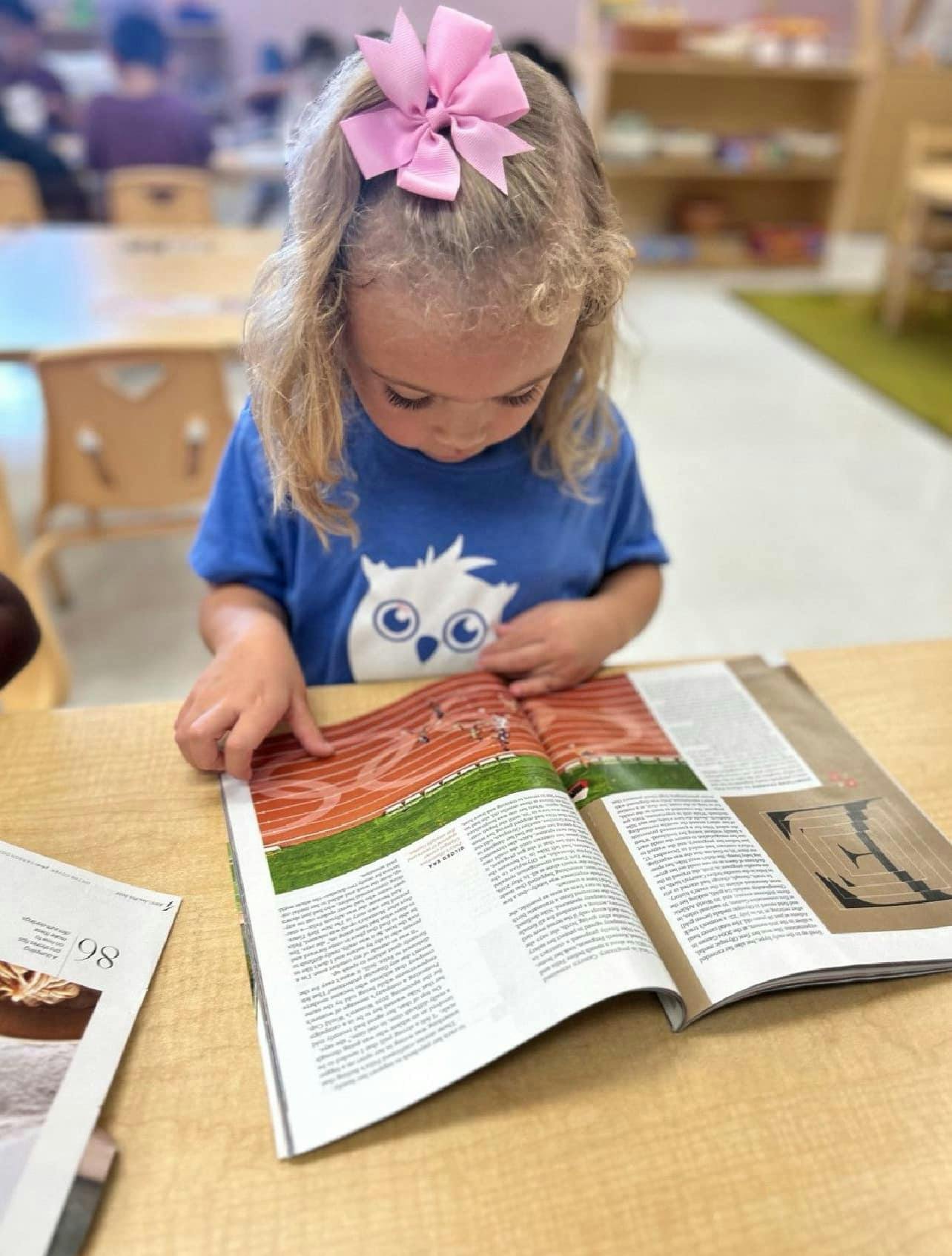Child with pink bow looking at an open magazine on a table