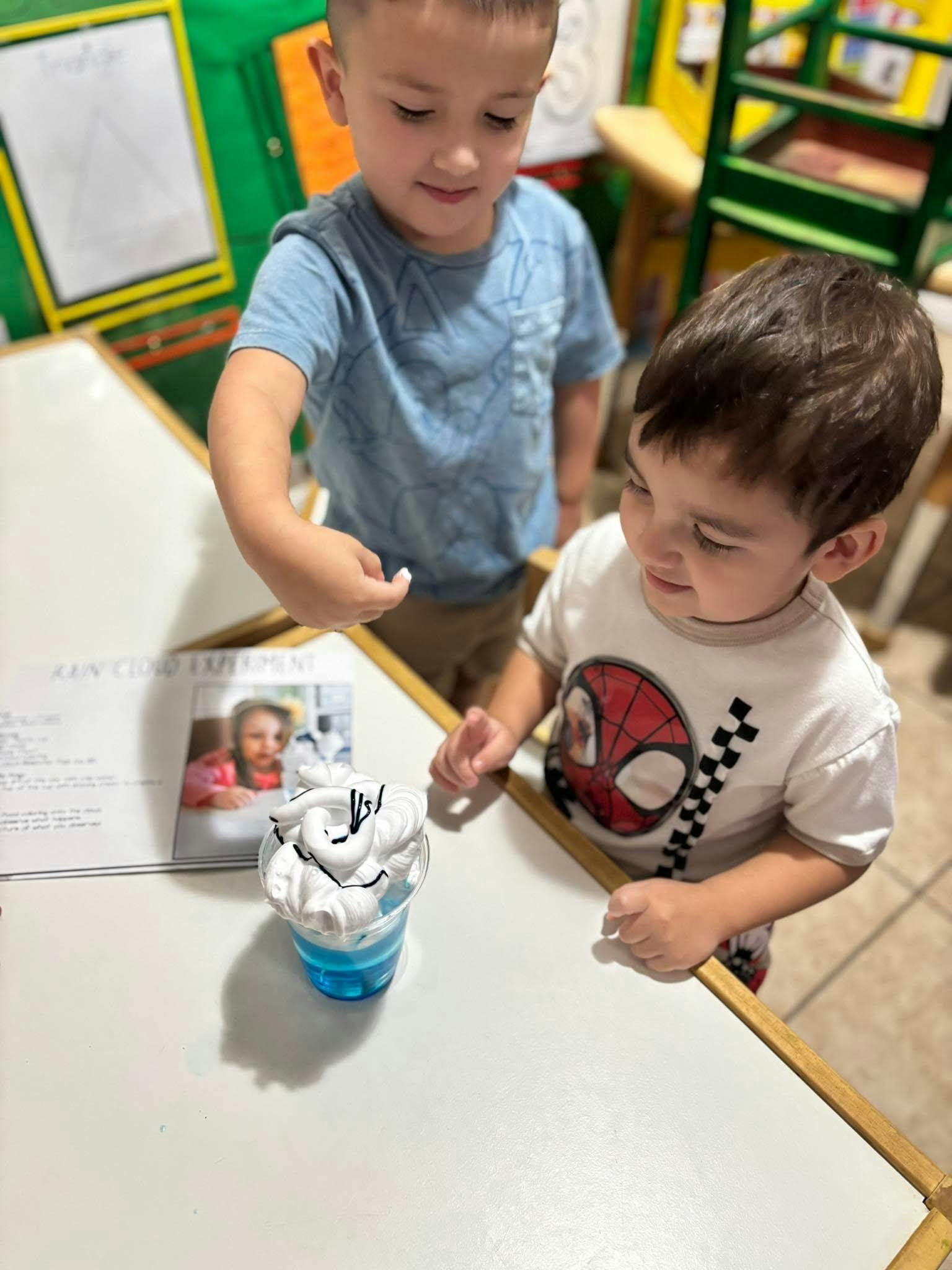 Two children observing a cup with blue liquid and shaving cream