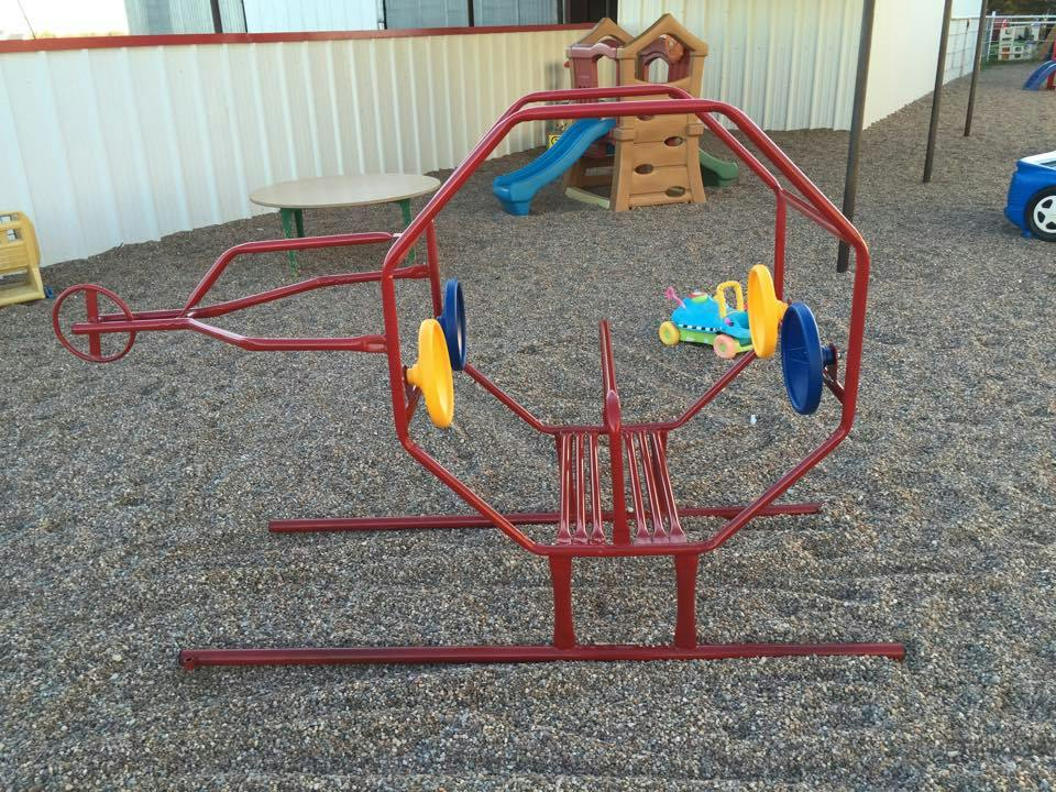 Red metal playground helicopter ride on a gravel surface