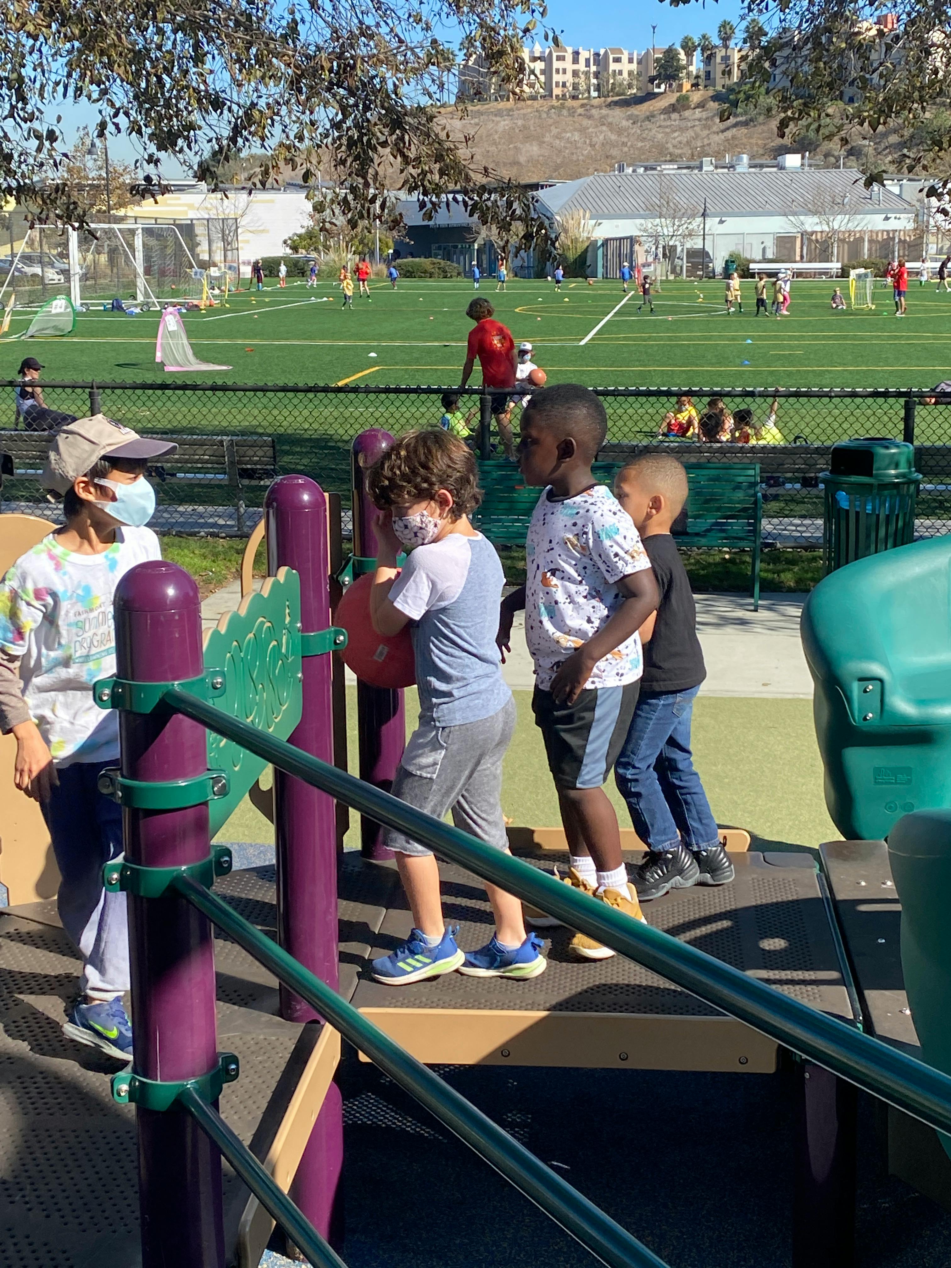 Children on a playground structure with a sports field in the background