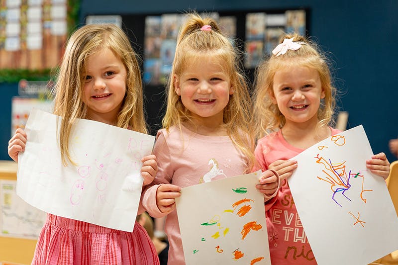 Three children holding up drawings