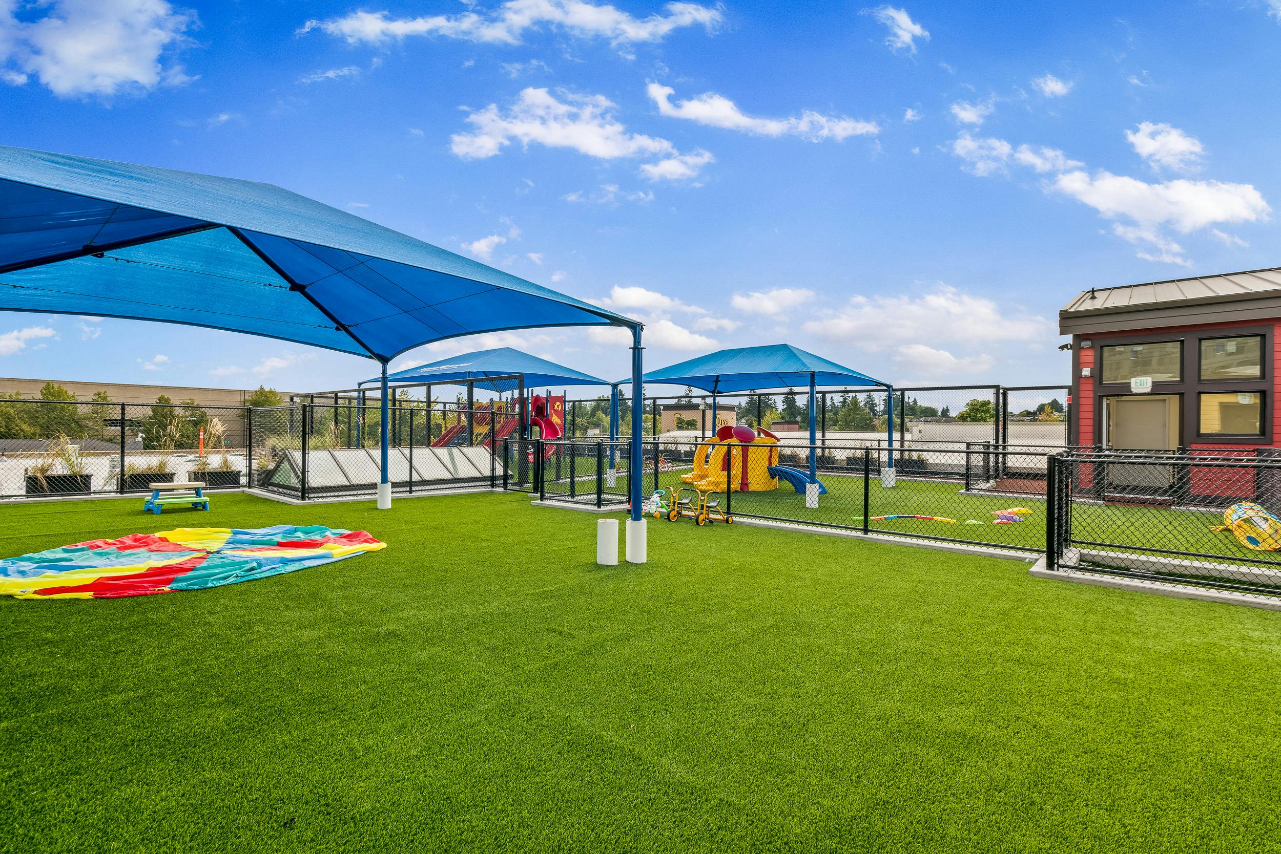 Outdoor playground with artificial turf, blue shade structures, and play equipment