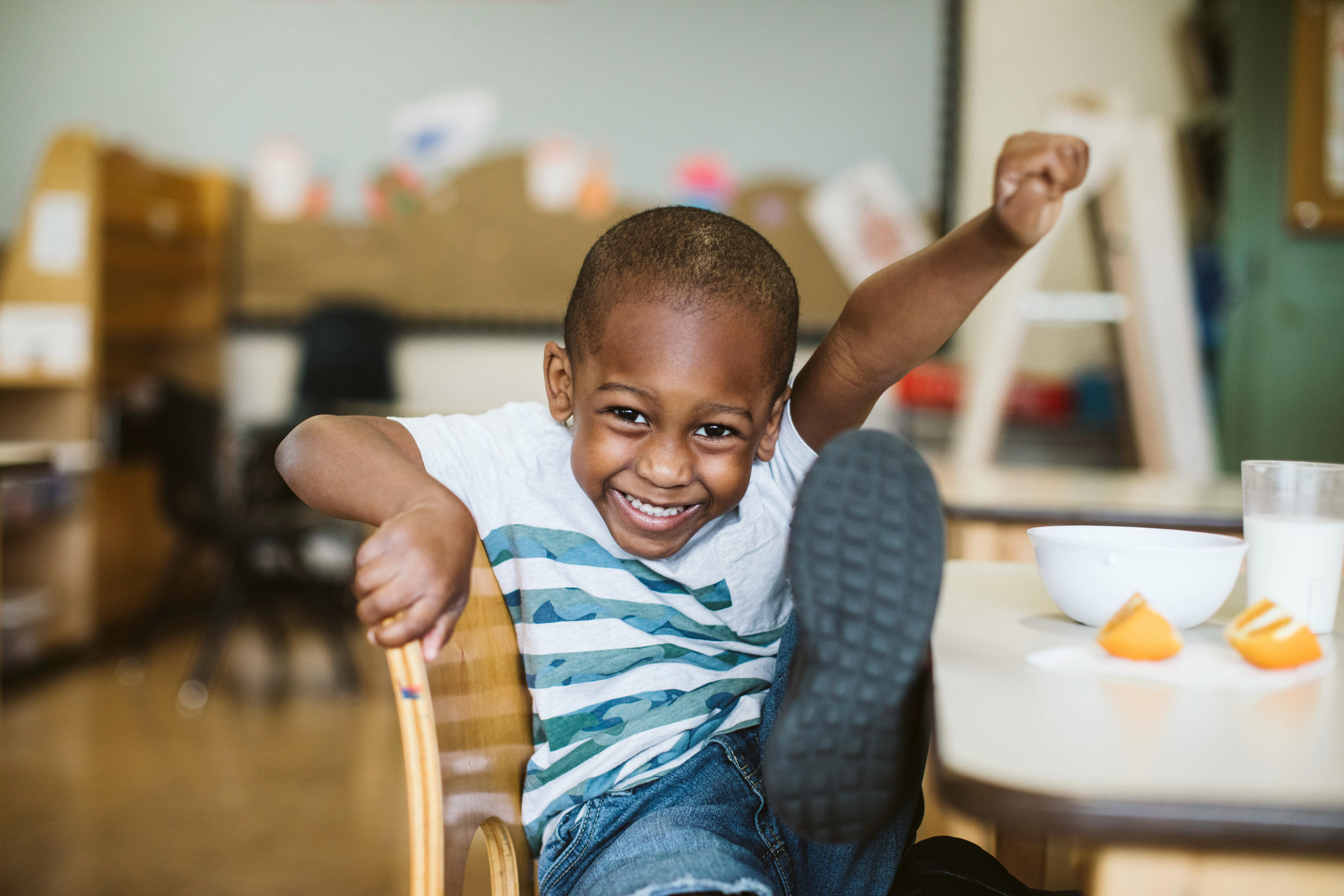 Child sitting at a table with one arm raised and one leg up