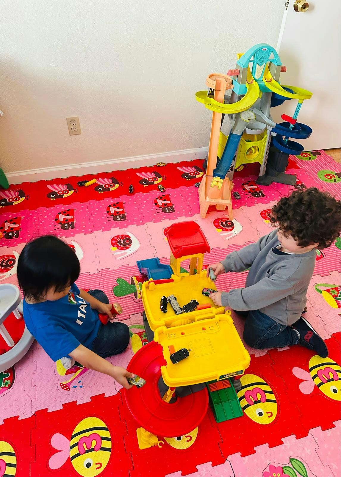 Two children playing on the floor with toy cars and a playset
