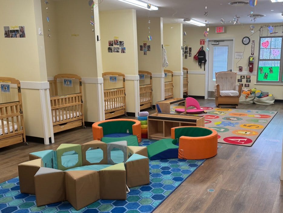 A colorful daycare room with cribs, play mats, and soft play furniture
