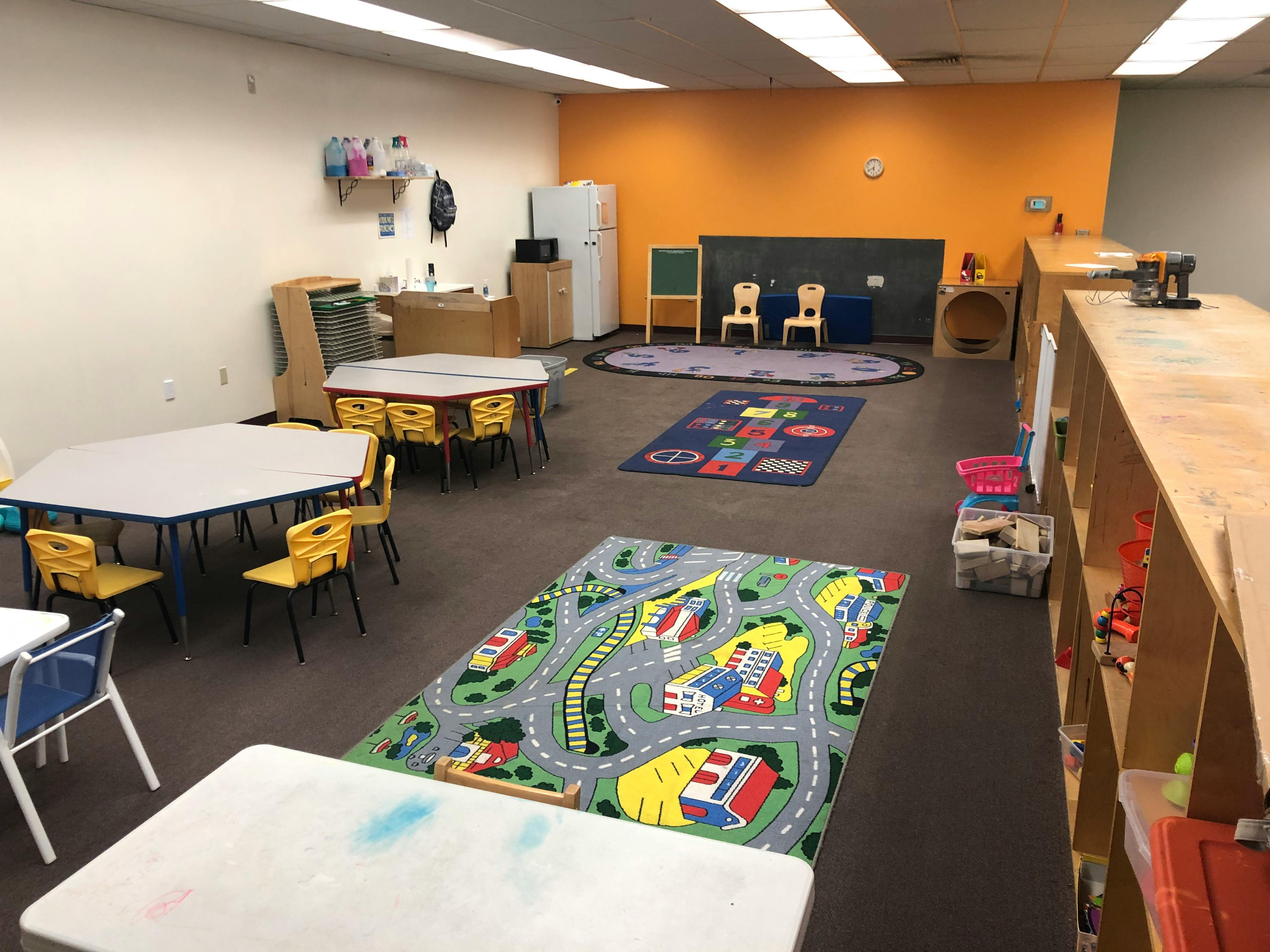 Empty classroom with small tables, chairs, and play rugs