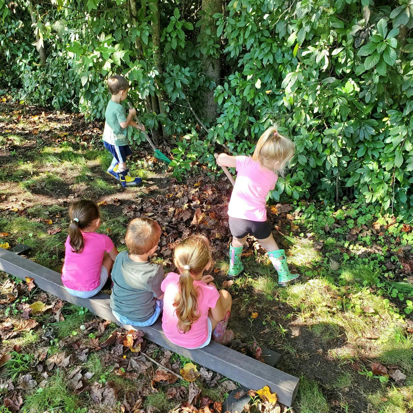 Children playing outdoors, one child raking leaves, three children sitting on a beam