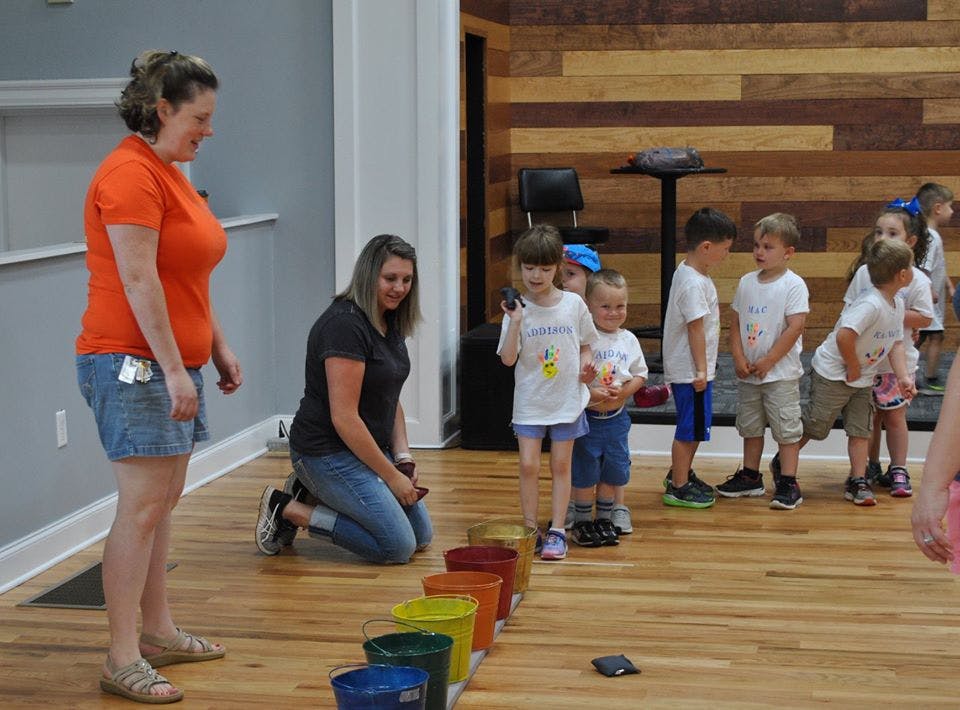 Two adults supervising a line of children standing behind colorful buckets