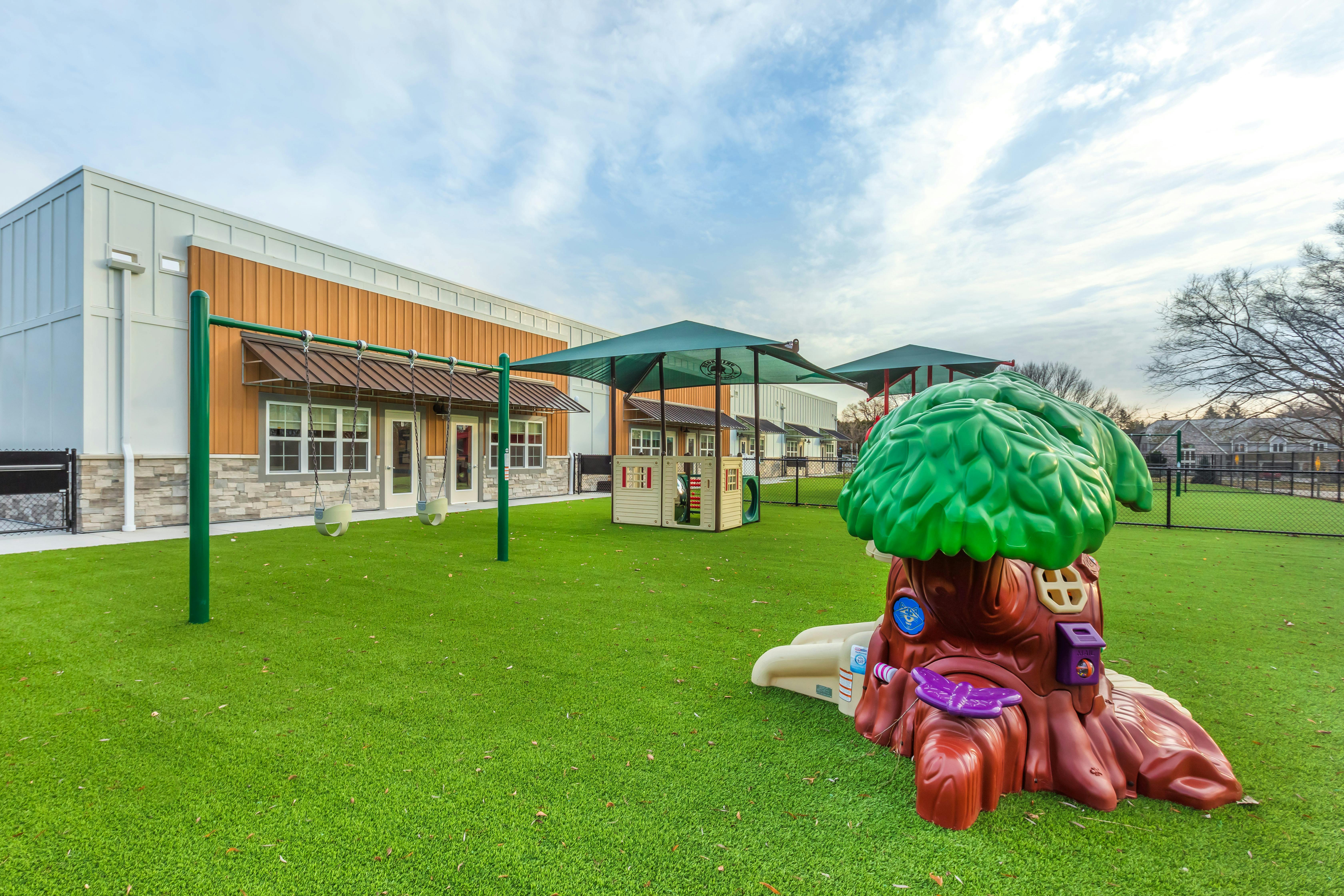 Playground with swings, playhouses, and an artificial turf lawn next to a building