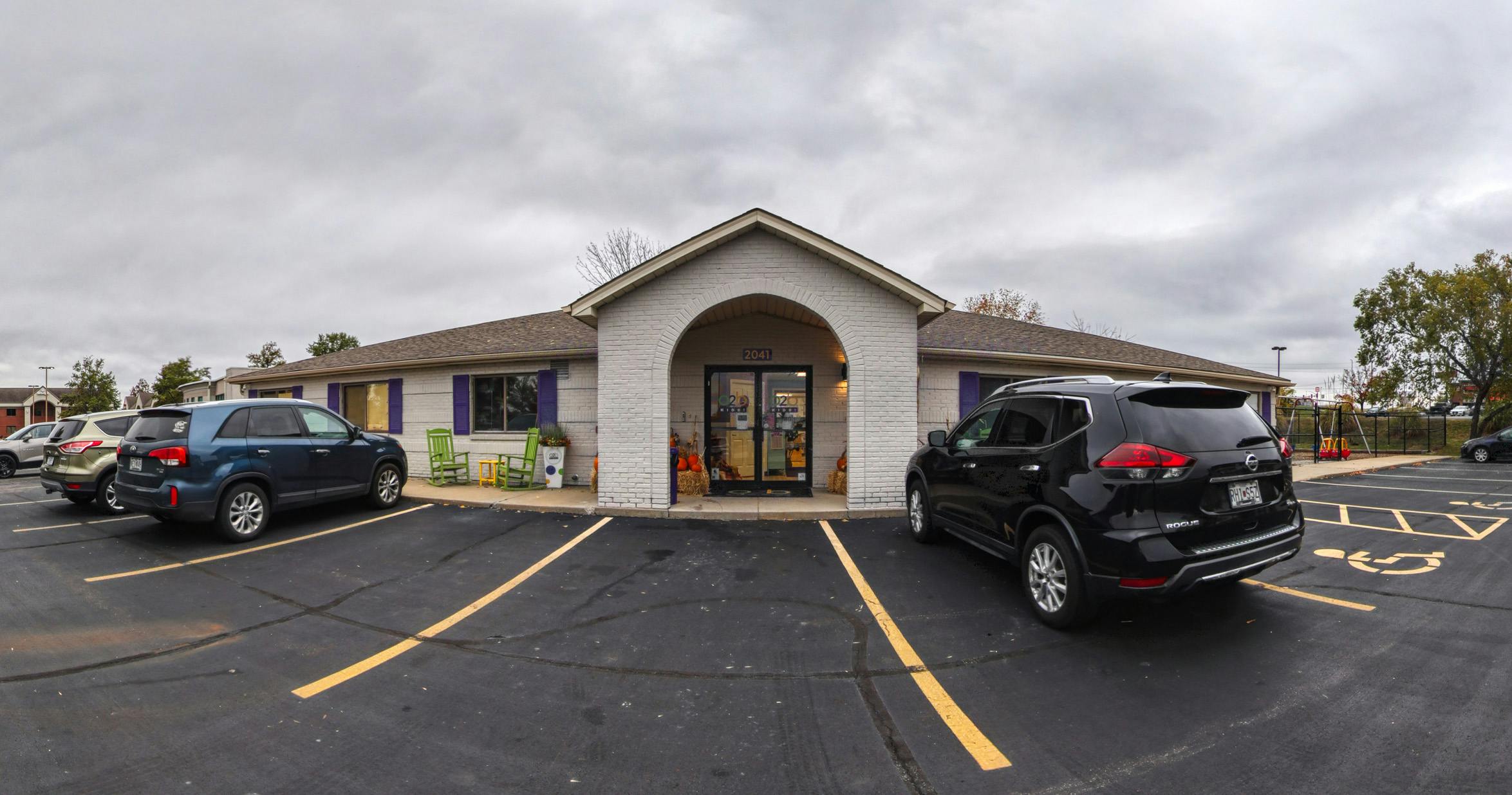Building exterior with a small arched entryway, two parked cars, and a playground swing set