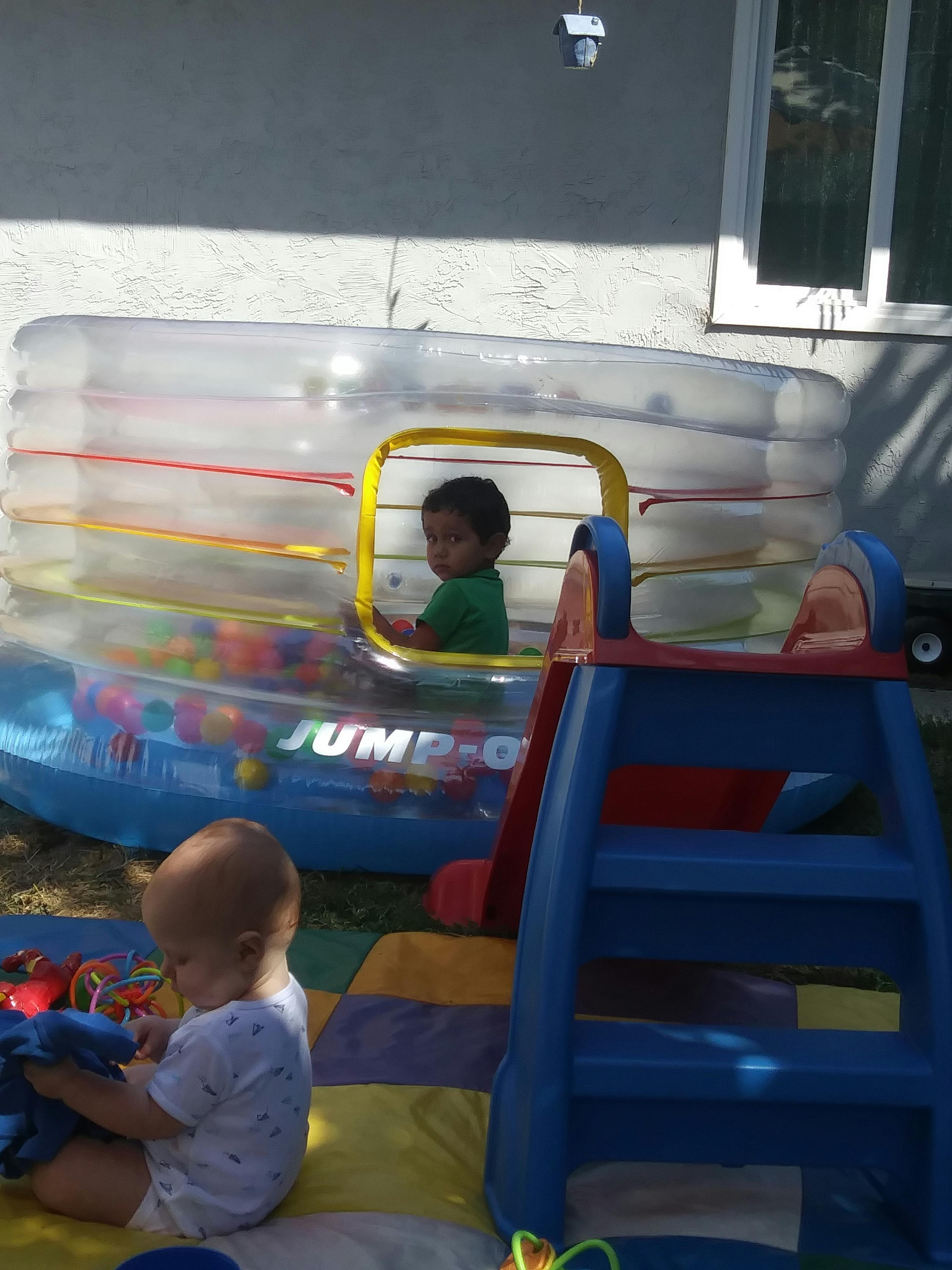 Child in an inflatable ball pit and another child playing on a mat