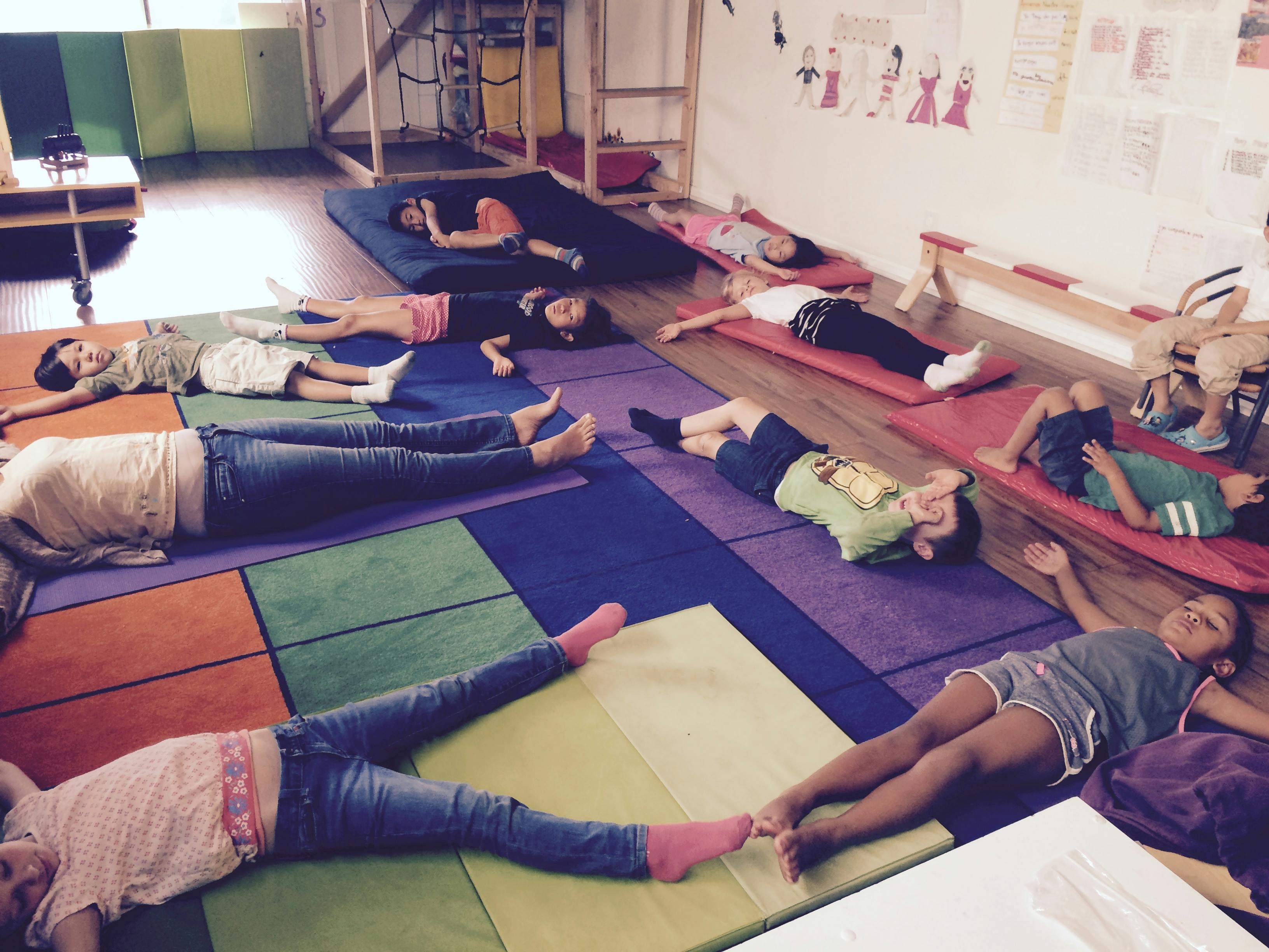 Several children and adults resting on mats on the floor