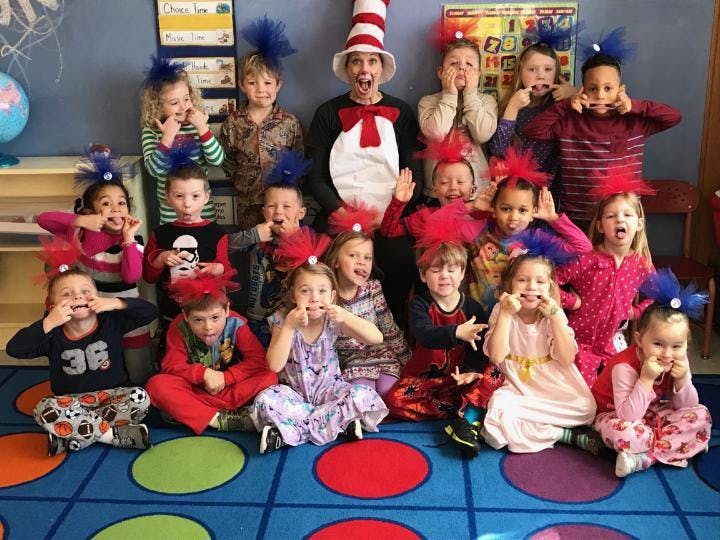 Person in a striped hat with many children making silly faces in a classroom