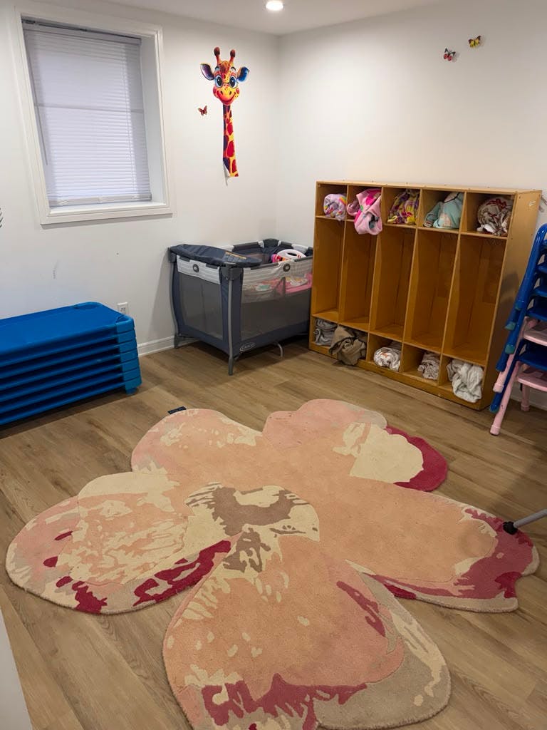Childcare room with a playpen, cubby shelves, and a large flower-shaped rug
